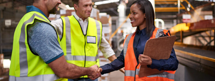 Shot of two workers shaking hands together while standing in a large warehouse