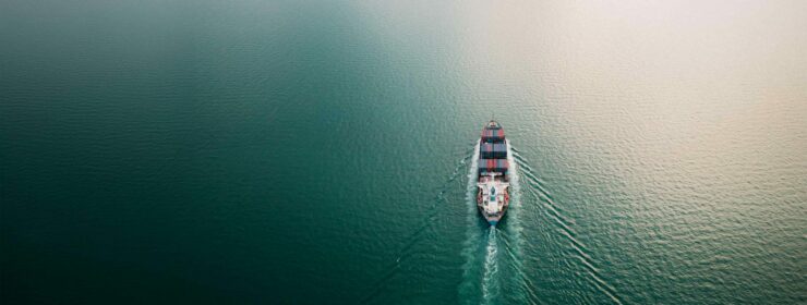 business services import export international by containers ship sailing on green sea and over the sun light background aerial view