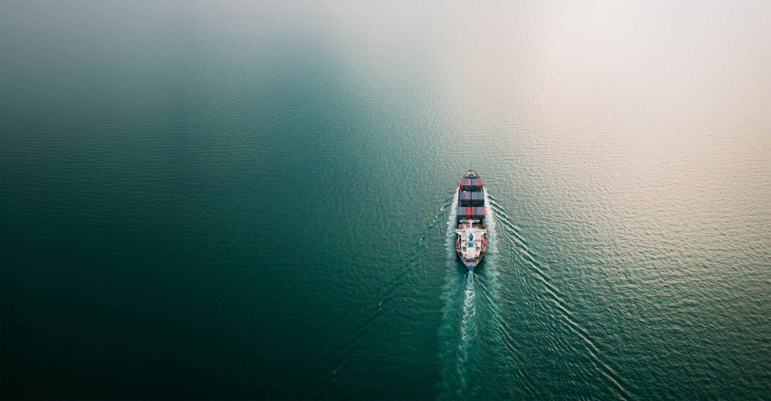 business services import export international by containers ship sailing on green sea and over the sun light background aerial view
