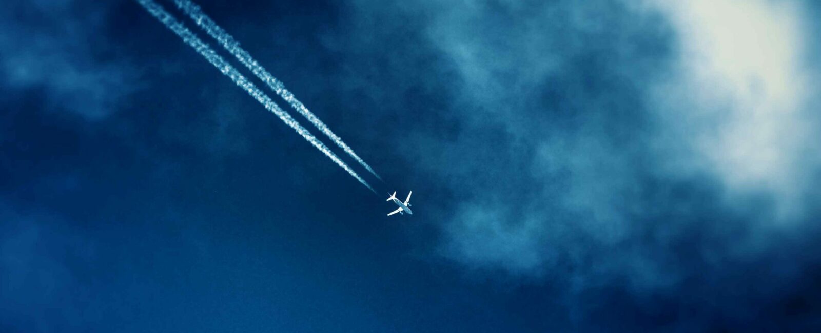 Airliner track in the clouds in the dark blue sky seen from the bottom in the afternoon