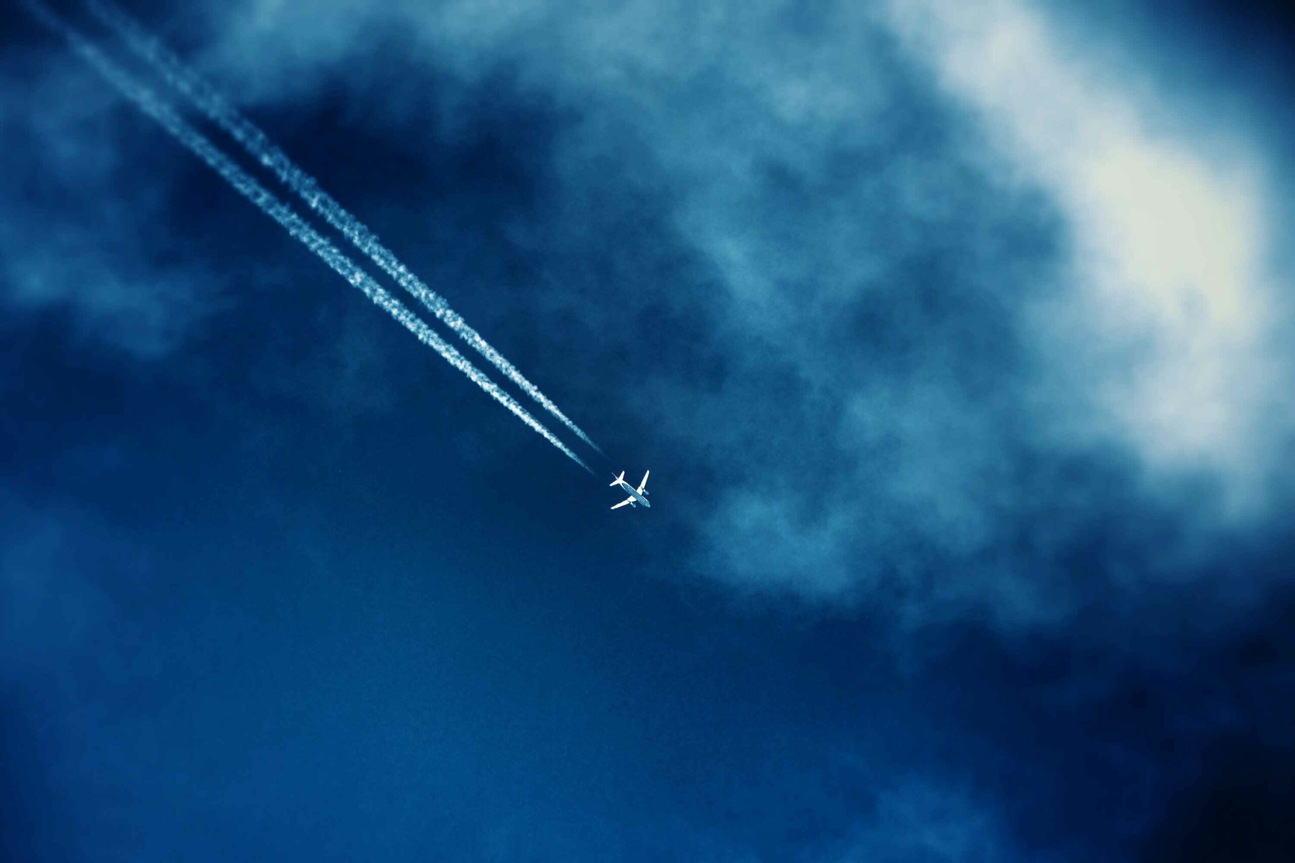 Airliner track in the clouds in the dark blue sky seen from the bottom in the afternoon