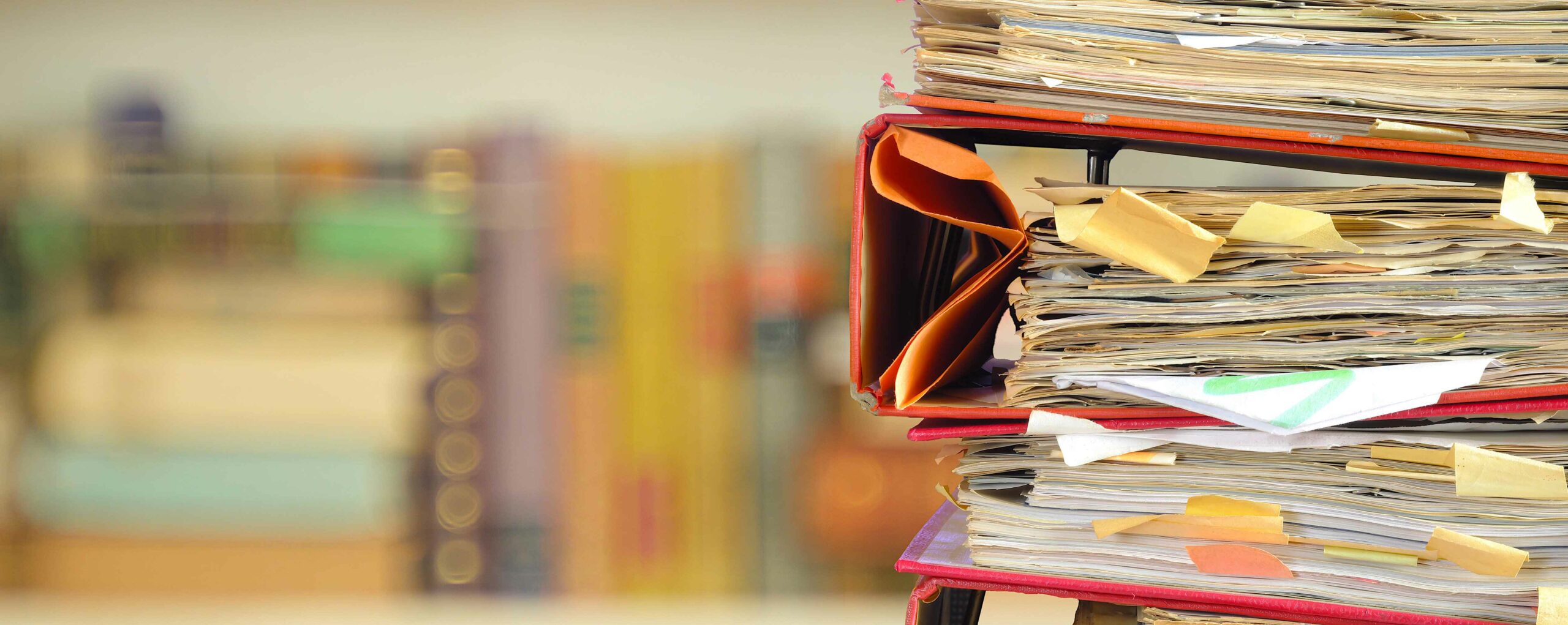 stack of messy file folders with narrow depth of field, blurred bookshelf in the back