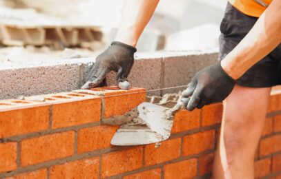 hands of Bricklayer with Masonry Trowel laying bricks on mortar