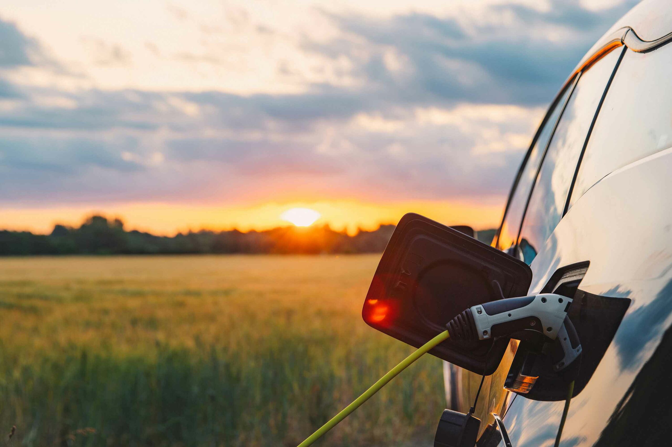 An electric car plugged in against a background of a rural location at sunset