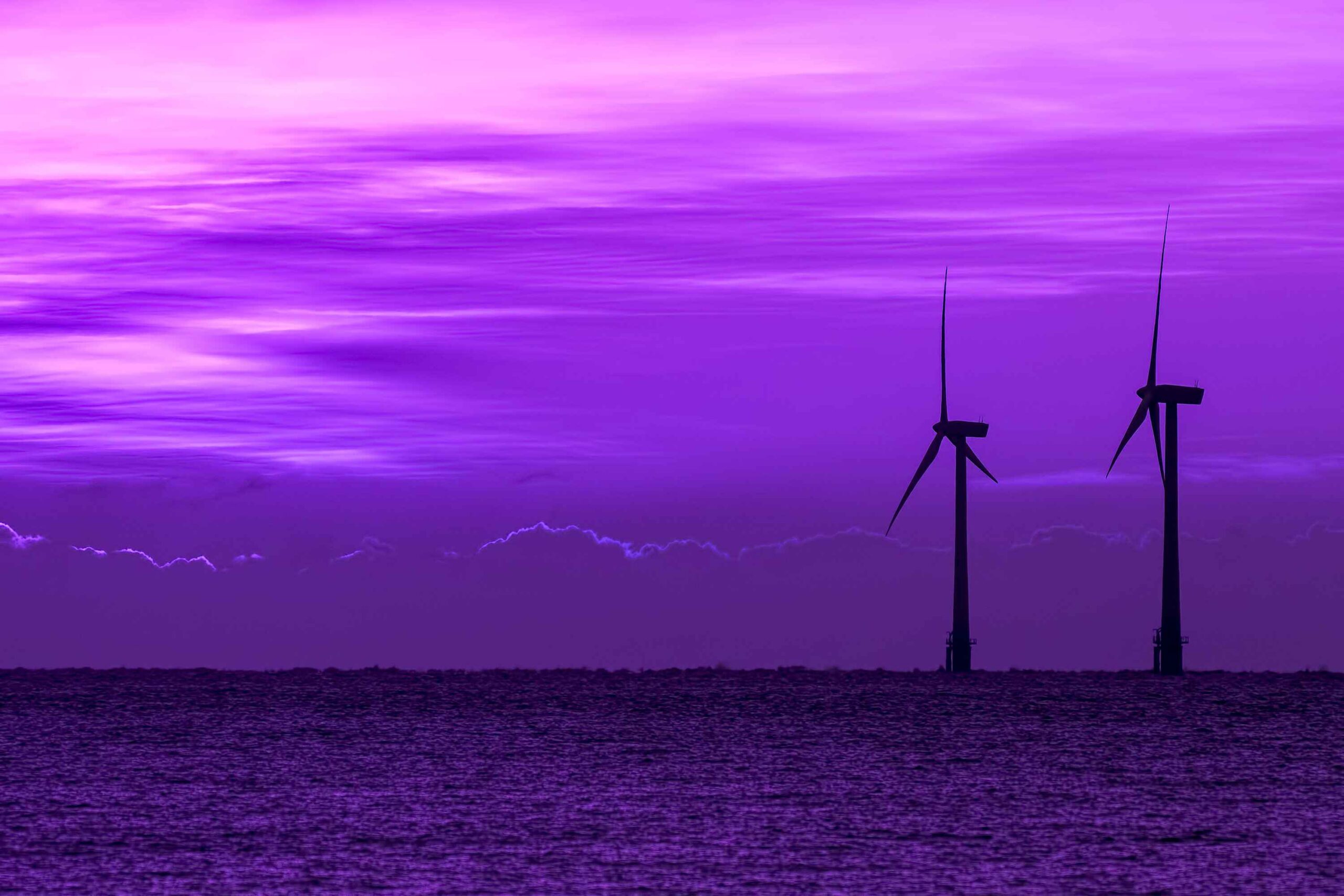 Surreal purple sky at twilight with silhouette of wind turbines on the sea horizon