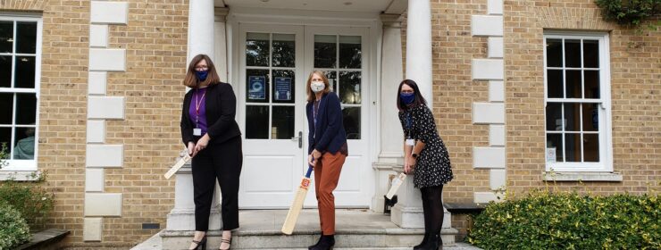 Staff on the steps of the Chelmsford office with cricket bats for charity