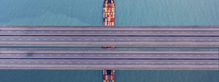 Container freight ship passing under bridge